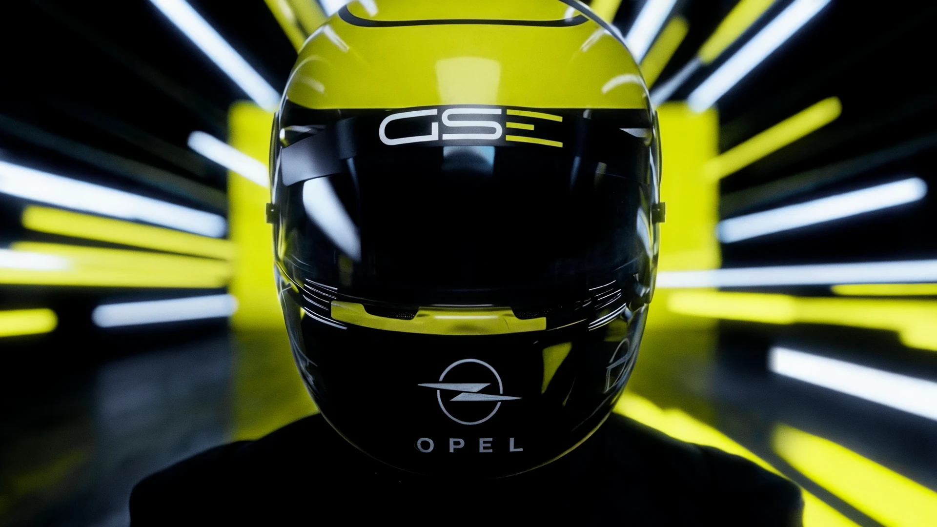 Frontansicht eines gelb-schwarzen Opel GSe Rennhelms mit Opel-Logo und Markenname, vor einem Tunnel aus gelben und weißen Neonlichtstreifen.