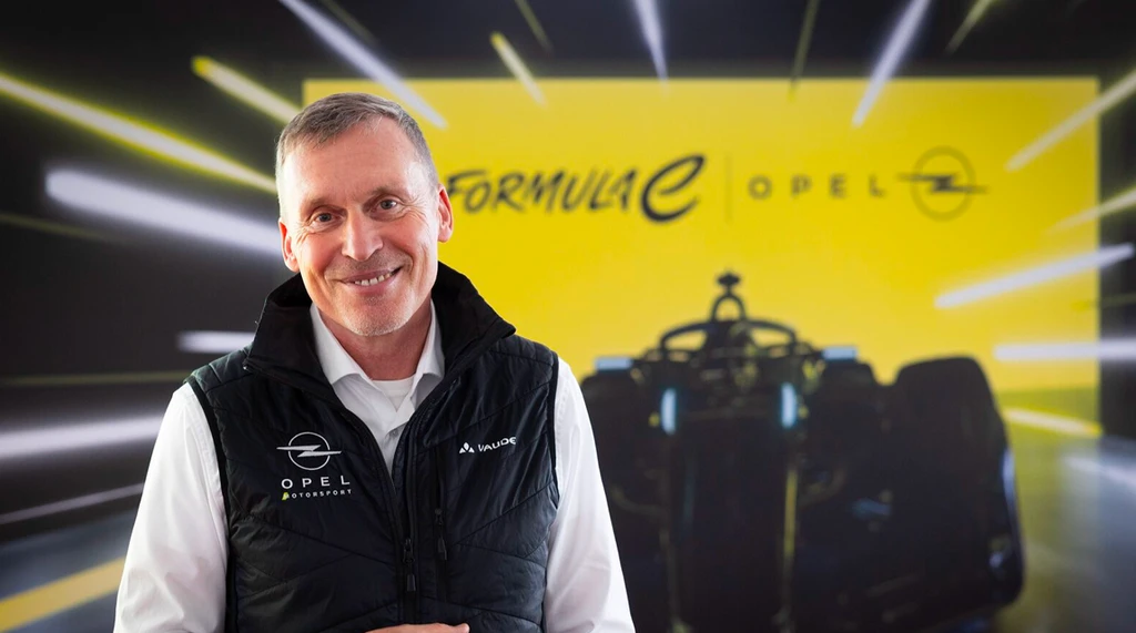Porträt von Jörg Schrott, Teamchef des Opel GSE Formula E Teams und Direktor des Opel Motorsports, lächelnd mit verschränkten Armen, in einem weißen Hemd, vor einem hellgrauen Hintergrund fotografiert.
