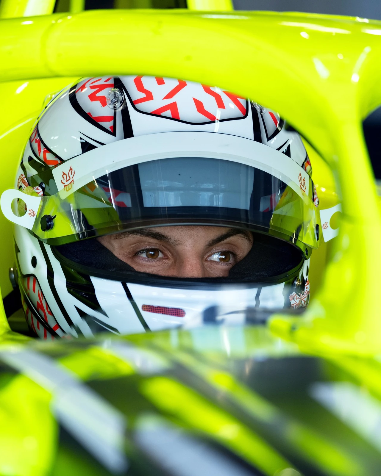 Close-up of a driver seated in the cockpit of the neon yellow Opel GSE Formula E car, wearing a white, red and black helmet with the visor raised, framed by the car's halo and bodywork.