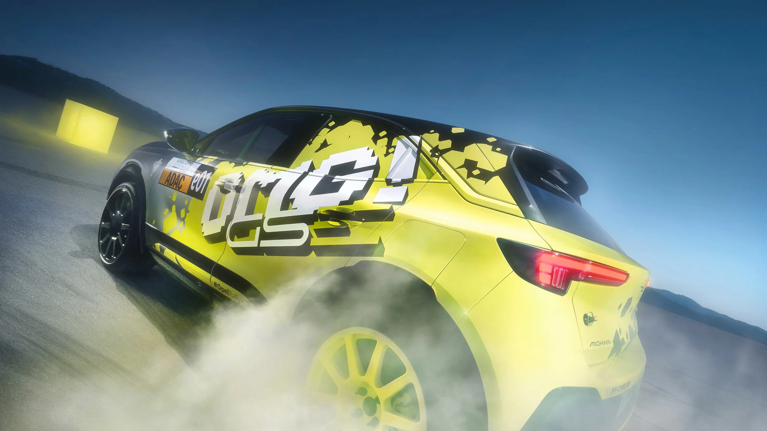Neon yellow and black Opel Mokka GSE rally car in bold "OMG GSE" livery, seen from behind at an angle while drifting and throwing up a cloud of dust, against a deep blue evening sky.