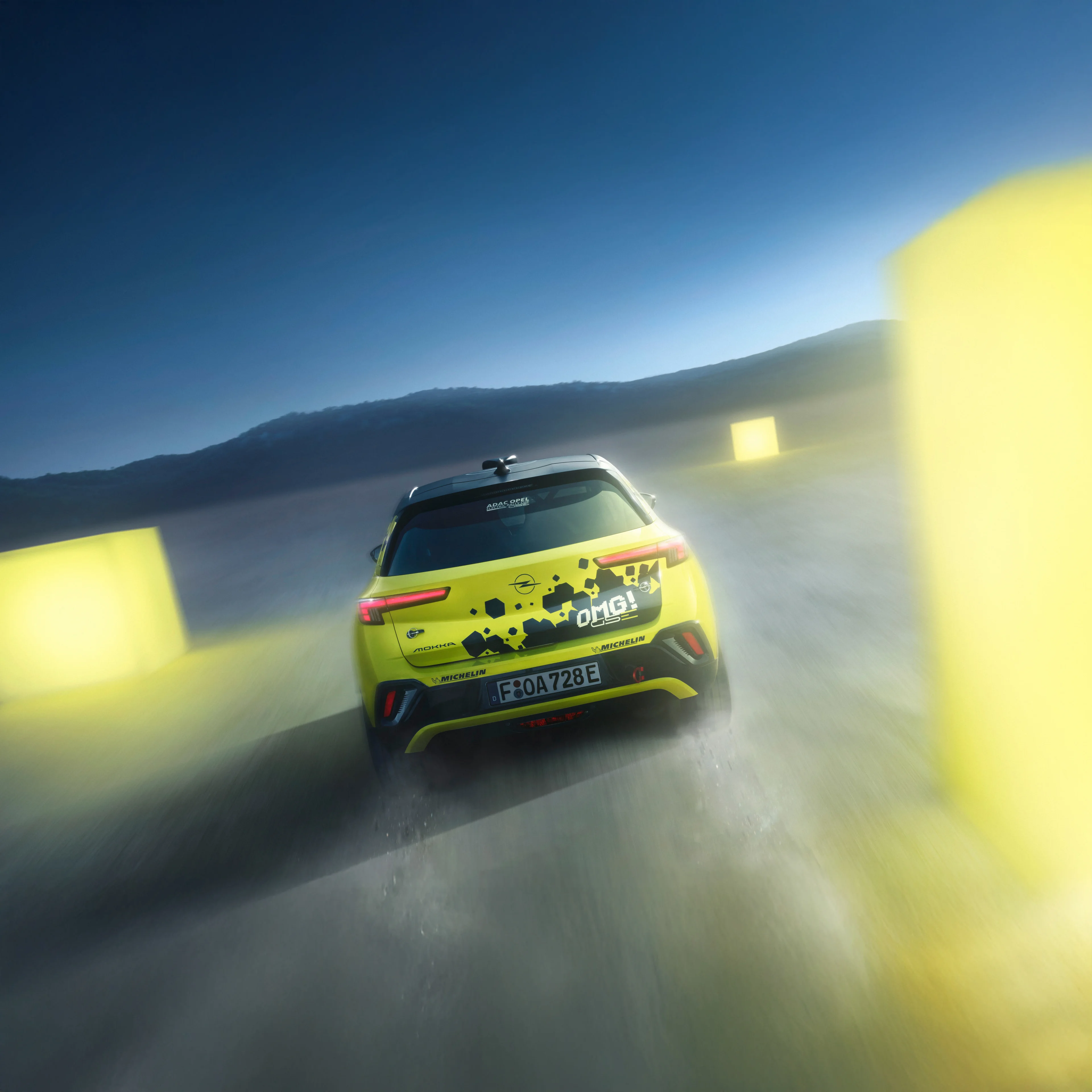 Neon yellow Opel Mokka GSE Rally car seen straight from behind driving away at dusk, tail lights lit, with yellow course markers blurred past on either side and a dark ridge on the horizon.